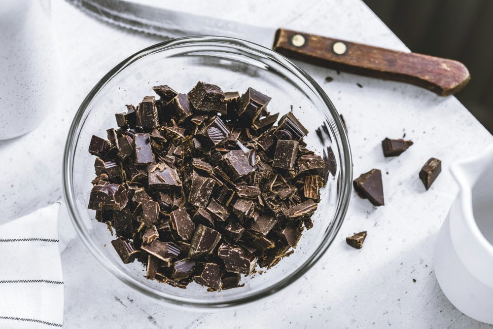 dark chocolate pieces chunked into glass bowl with knife alongside on countertop