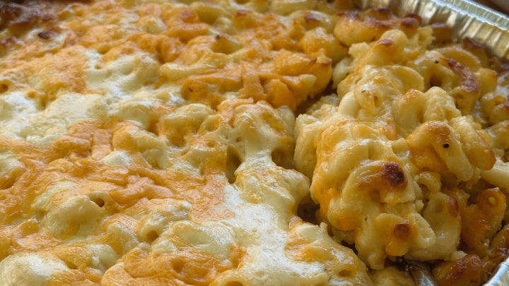 baked mac and cheese in large aluminum pan with spoon scooping out serving