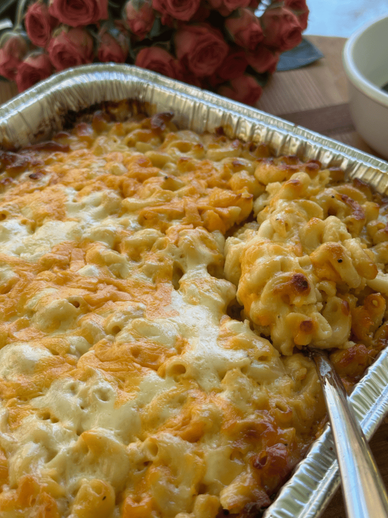 baked mac and cheese in large aluminum pan with spoon scooping out serving