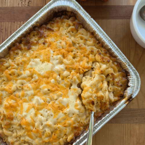 large pan full of creamy mac and cheese with spoon scooping out heaping portion, melty cheese