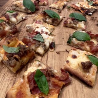 New Haven pizza in square pieces on wood cutting board - topped with prosciutto and basil
