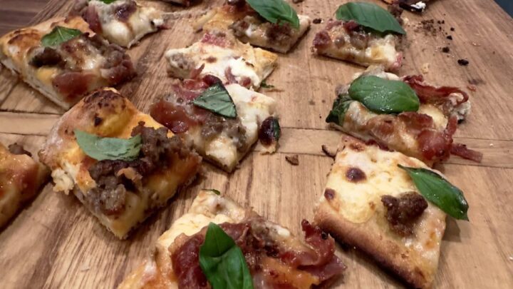 New Haven pizza in square pieces on wood cutting board - topped with prosciutto and basil