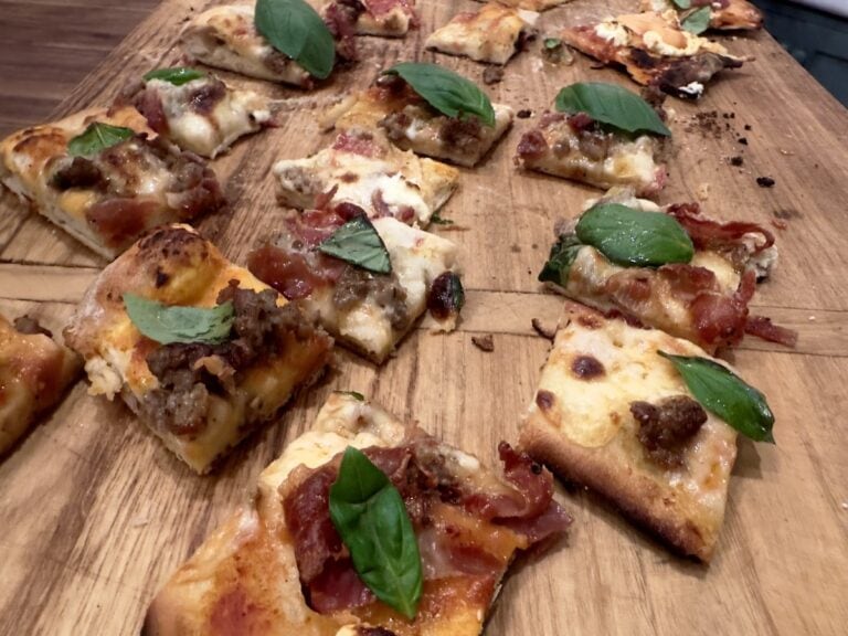 New Haven pizza in square pieces on wood cutting board - topped with prosciutto and basil