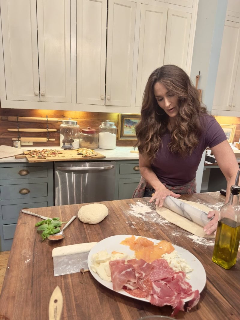 Stacy Lyn Harris making New Haven style thin crust pizza in kitchen, rolling out dough on butcher block table