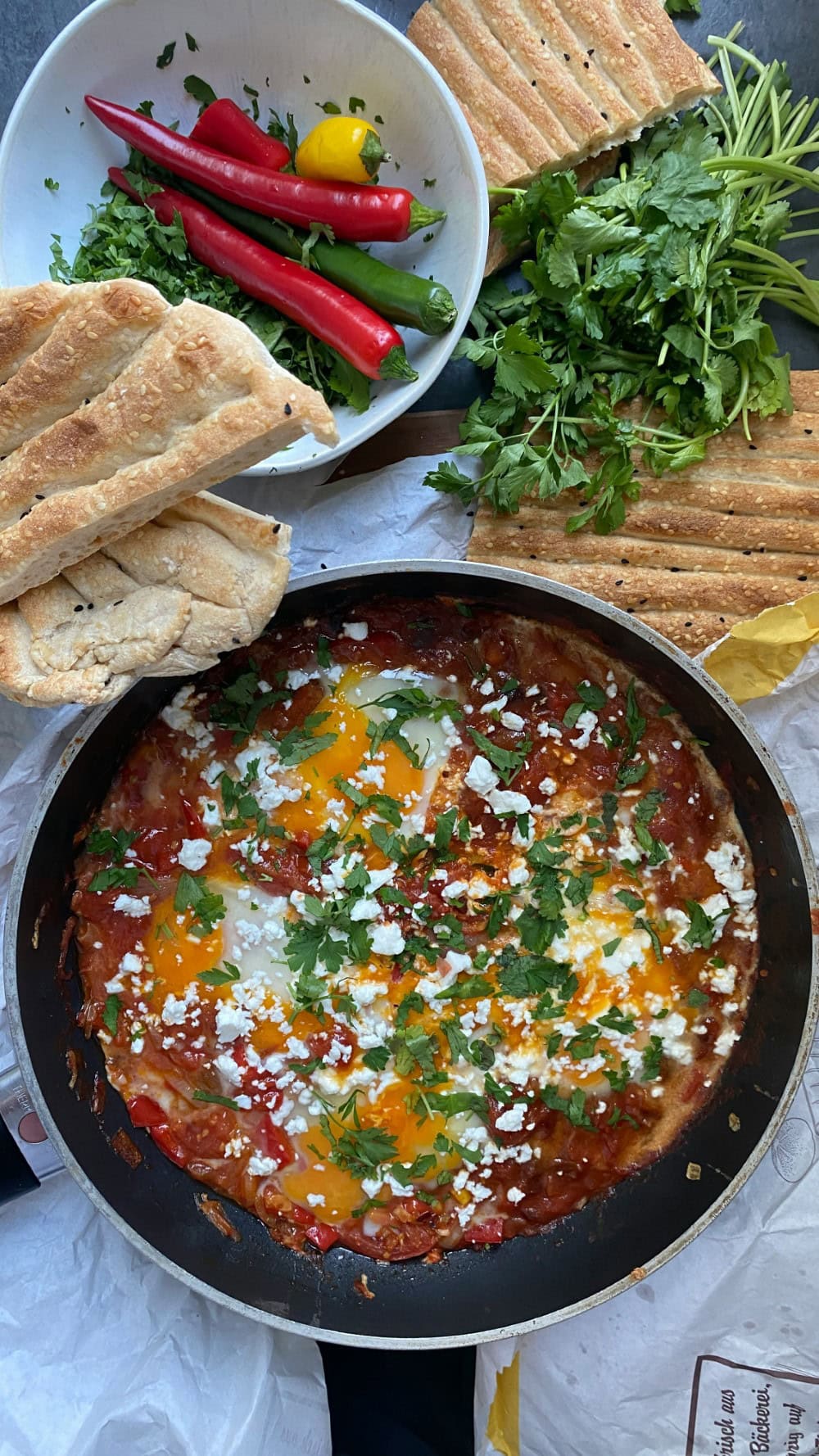 shakshuka in skillet surrounded by ingredients - red peppers, cilantro - and bread
