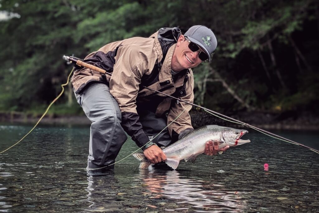 young man smiling while holding up salmon caught fly fishing in Alaska