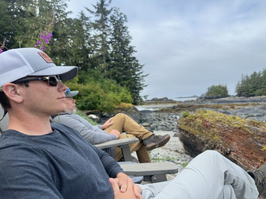 Howlett and Scott relaxing in chairs outside with tall trees in background