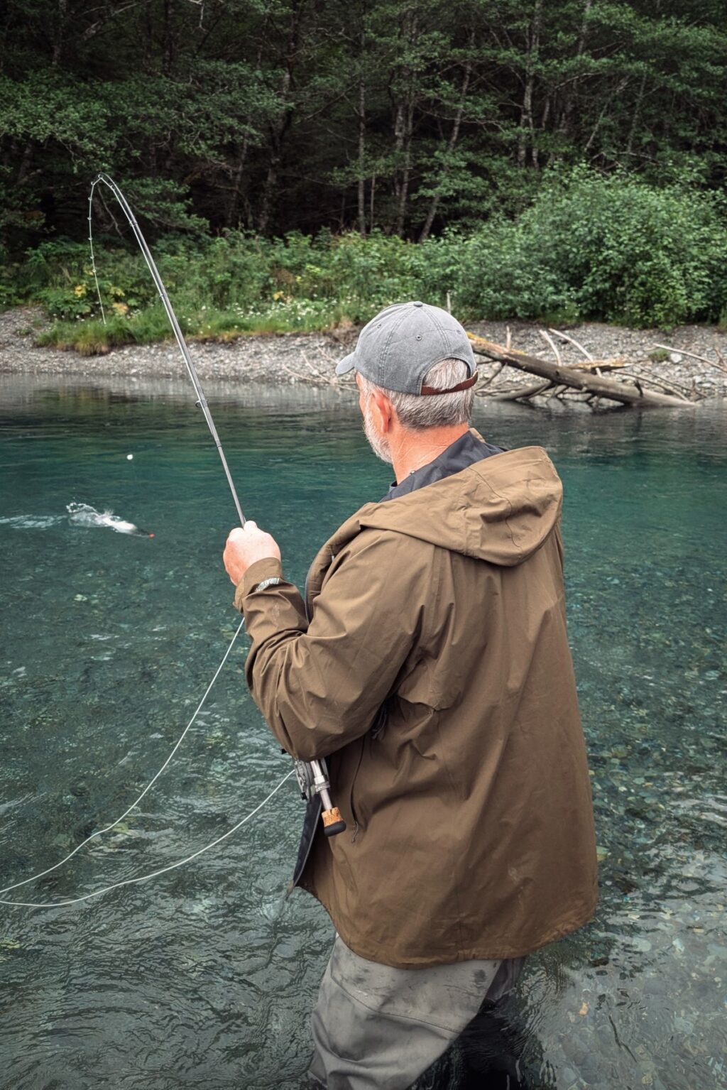 Man seen from behind while standing in river fly fishing in Alaska