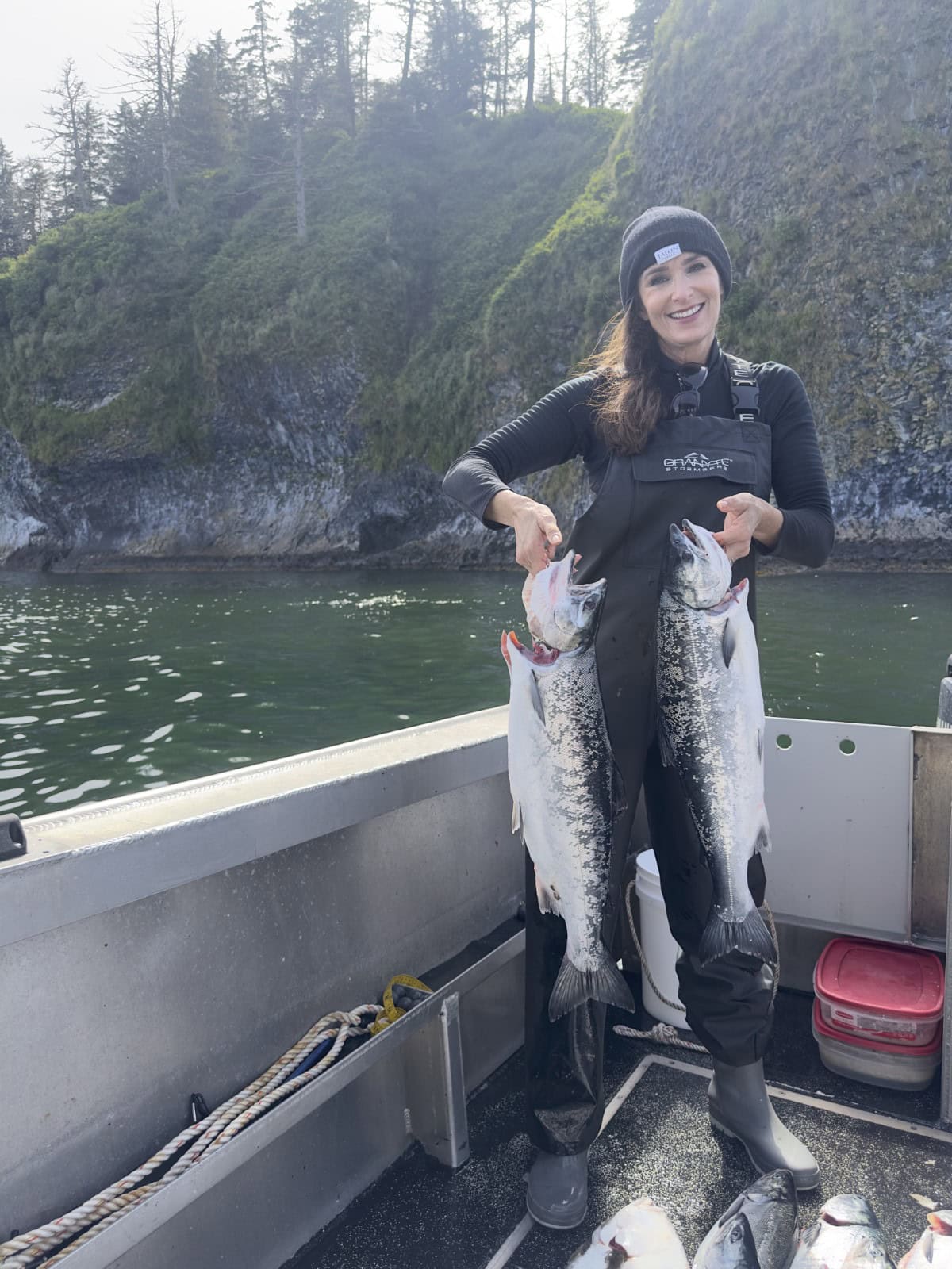 Stacy Lyn smiling on deep sea fishing boat while holding up two large fish she has caught
