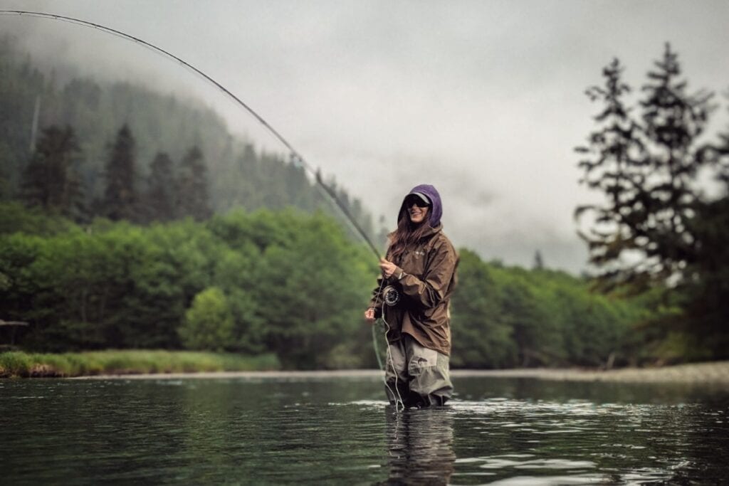 Stacy Lyn fly fishing in river near Sitka Alaska against lush green backdrop