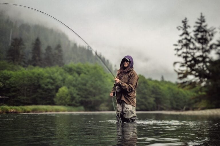 Stacy Lyn fly fishing in river in Sitka Alaska against lush green backdrop