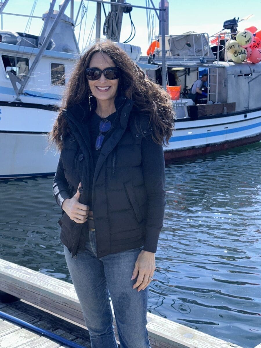 Stacy Lyn in dark blue jacket and sunglasses on pier in front of ferry boat in Sitka, Alaska