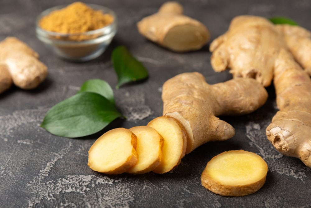 fresh sliced ginger and small cup of powdered ginger on stone countertop