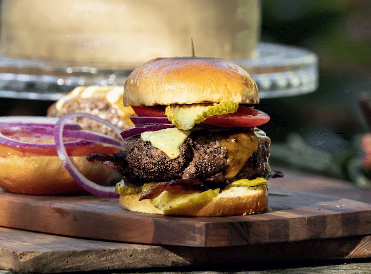 thick bacon pepper burger with fixins on rustic wooden cutting board
