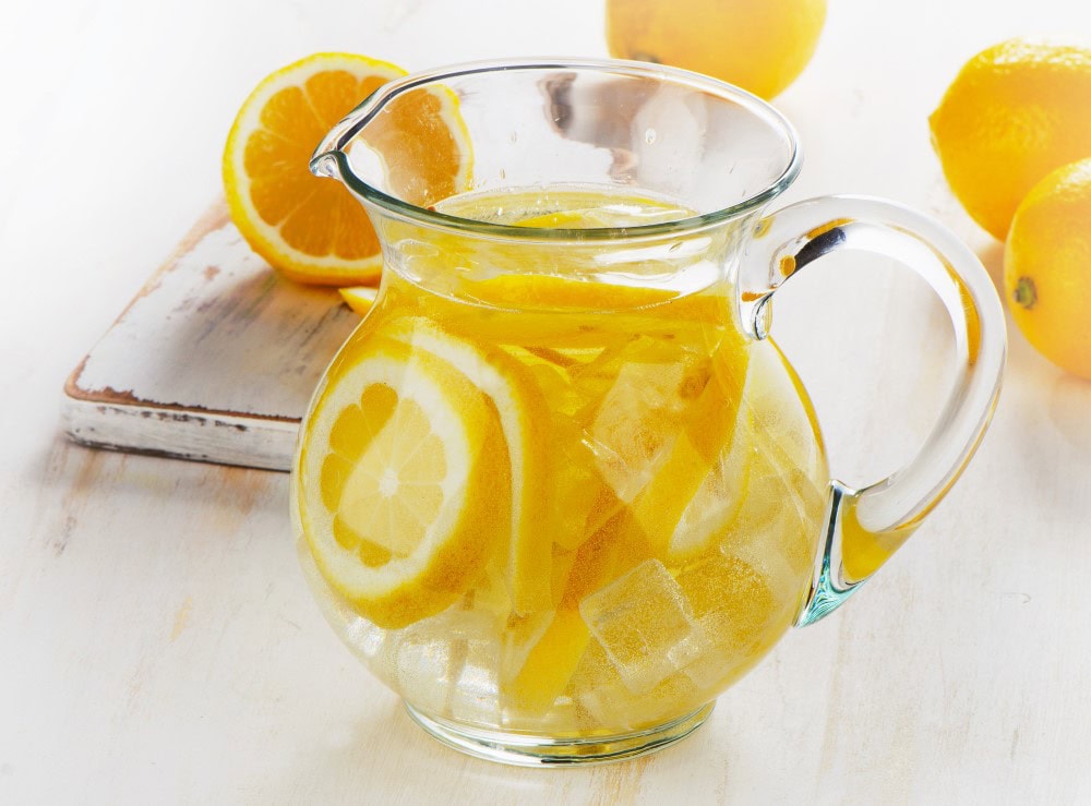 pitcher of lemon water with ice and sliced lemons in background on white counter