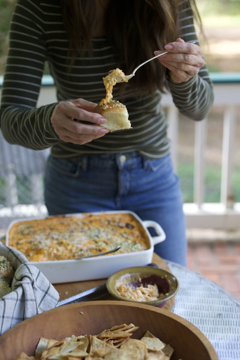 Stacy Lyn spooning buffalo chicken dip from casserole dish onto a fresh roll