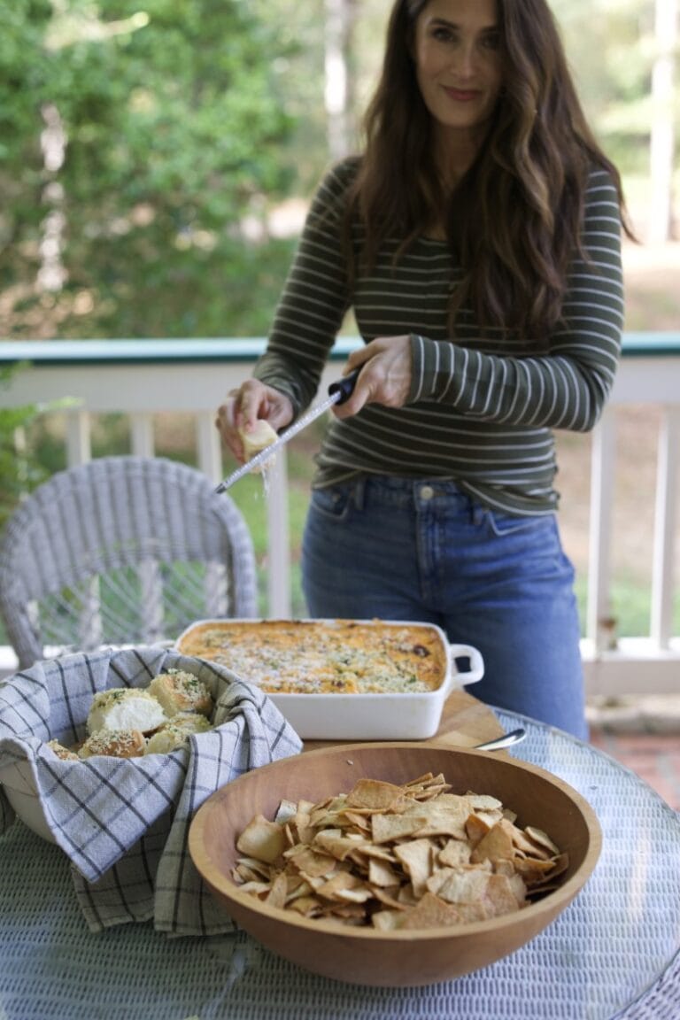 Stacy Lyn grating extra cheese onto baked buffalo chicken dip in white casserole pan