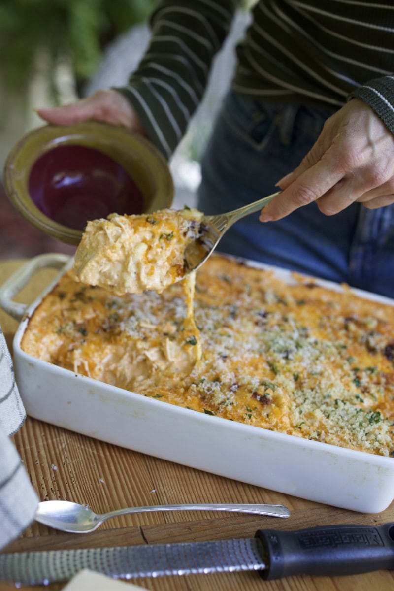 Stacy Lyn spooning creamy buffalo chicken dip from casserole pan into dish