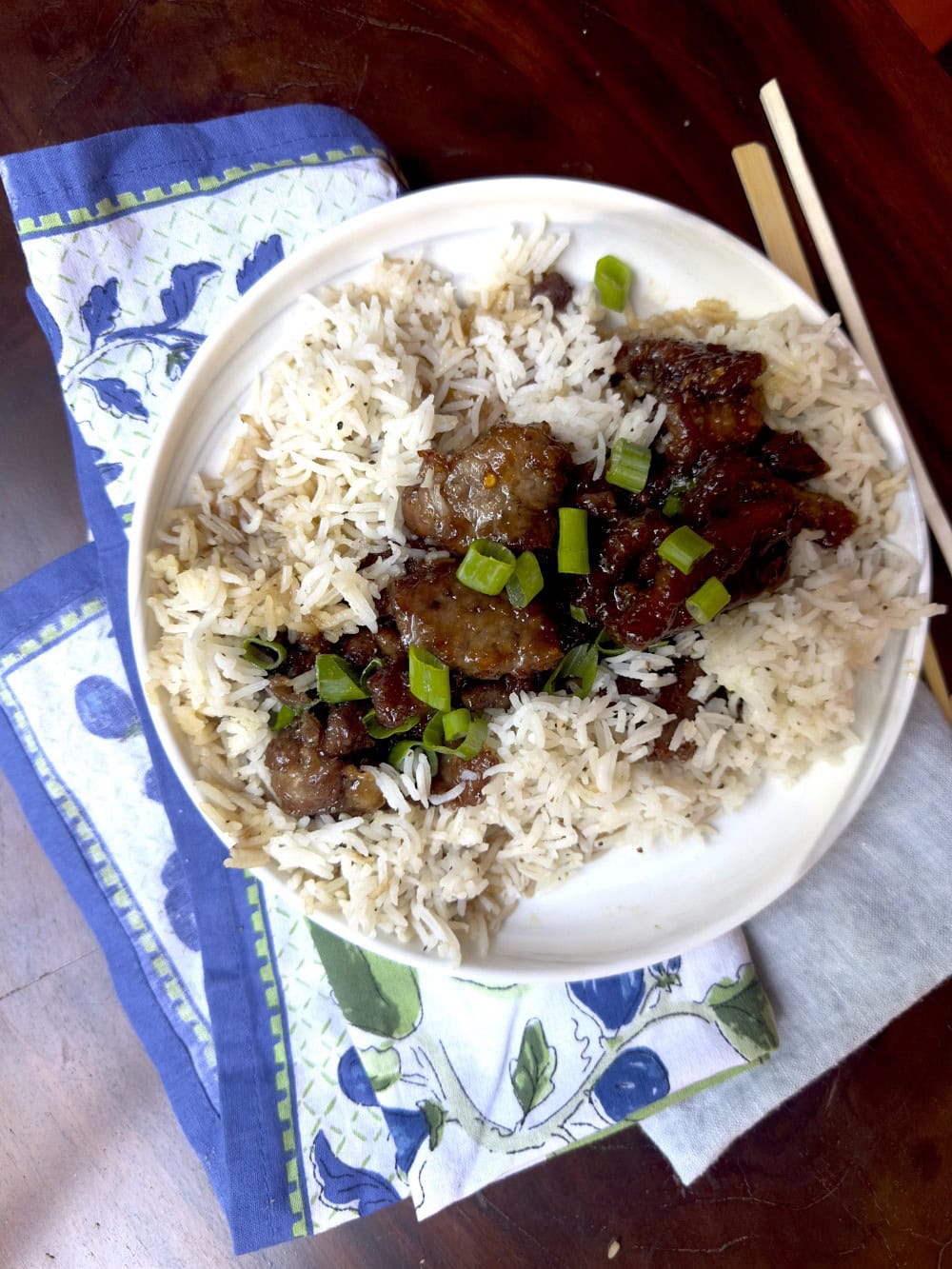 Stacy Lyn's Mongolian beef served on bed of rice on white plate atop blue floral napkins with chopsticks on side