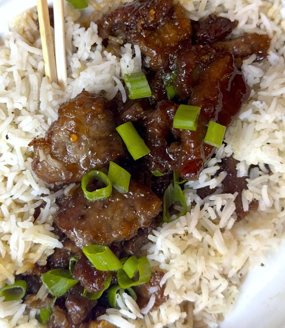 closeup of Mongolian beef served on bed or rice with garnish of green onions