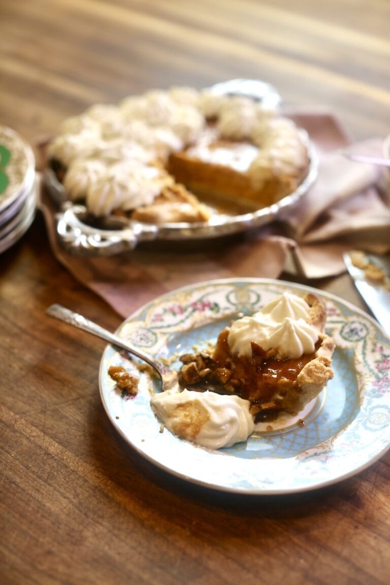 slice of pumpkin pie on floral china plate, topped with whipped cream - rest of pie in background