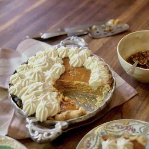 homemade pumpkin pie with maple whipped cream - slice on floral plate with rest of pie in pan behind it