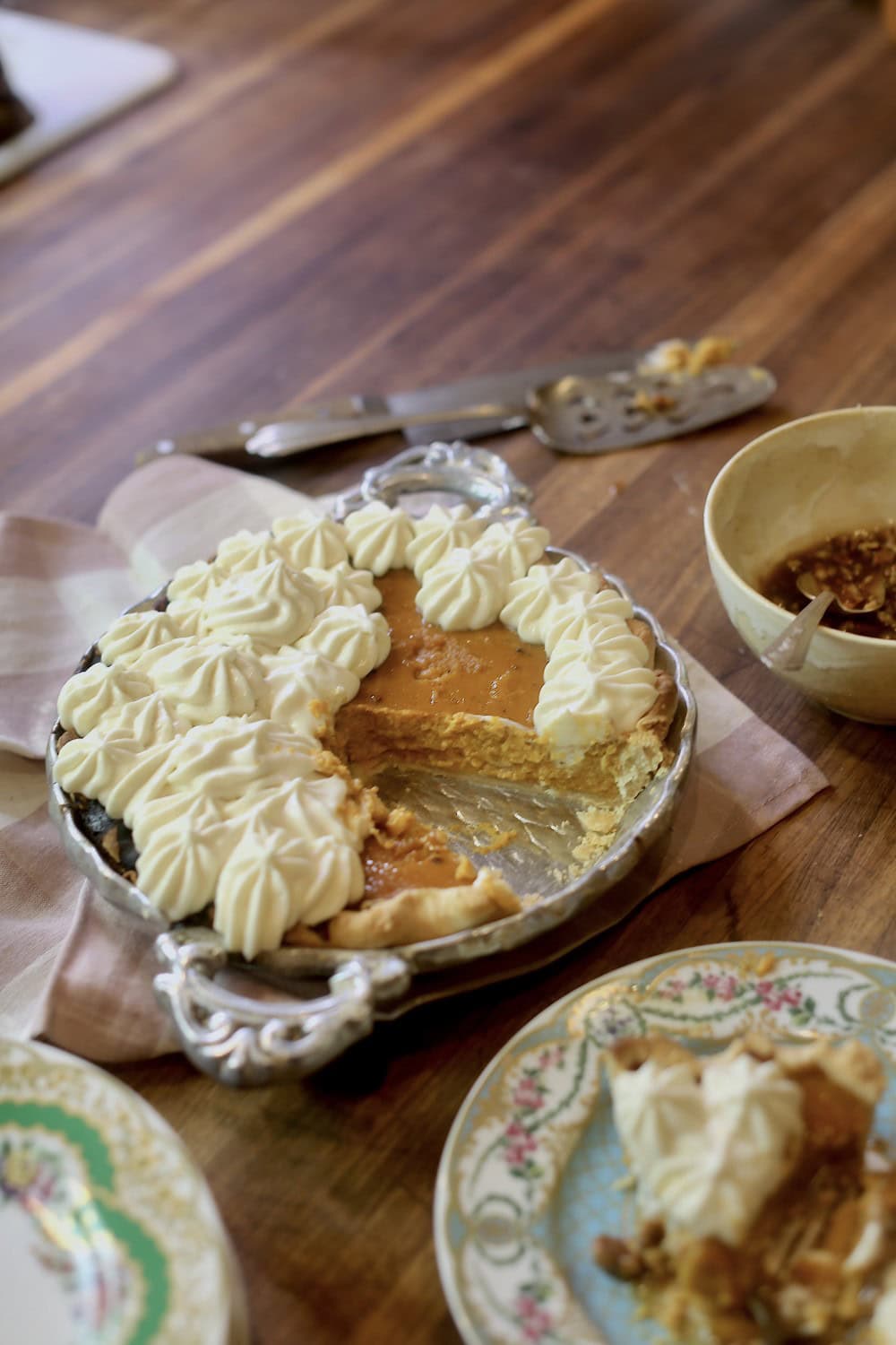 homemade pumpkin pie with maple whipped cream - slice on floral plate with rest of pie in pan behind it