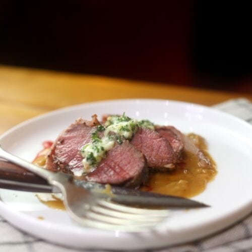 sliced venison backstrap loin served on white plate with herb butter and gravy
