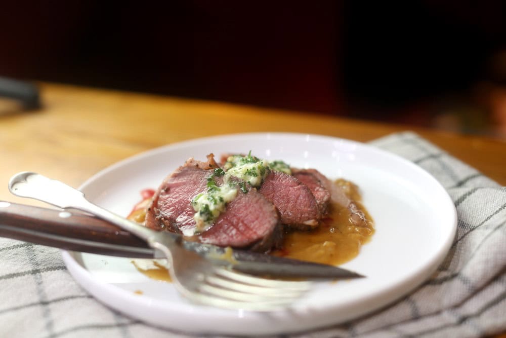 sliced venison backstrap loin served on white plate with herb butter and gravy