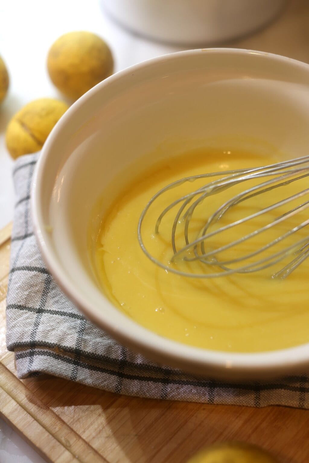 bright yellow lemon curd being whisked in large bowl with whole lemons in background