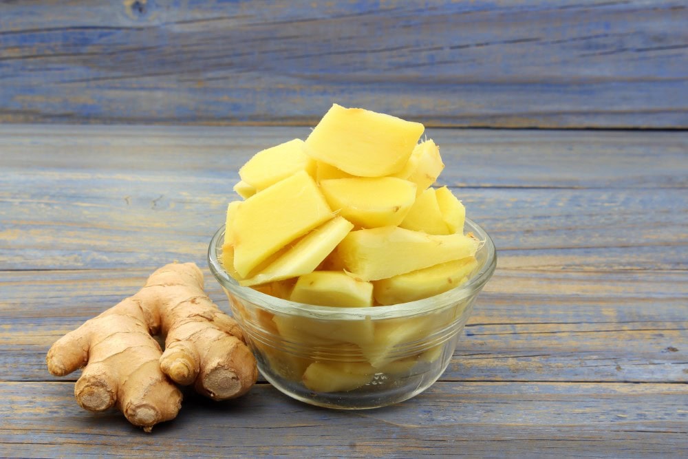 sliced peeled ginger in clear bowl next to whole ginger