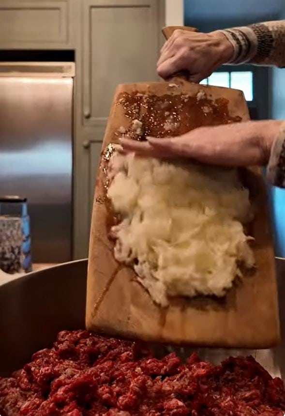 adding parmesan from cutting board to meat mixture