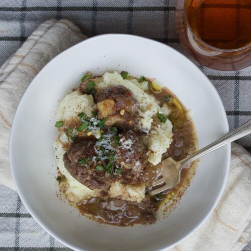 meatballs with meaty gravy served over mashed potatoes in white bowl on checked tablecloth
