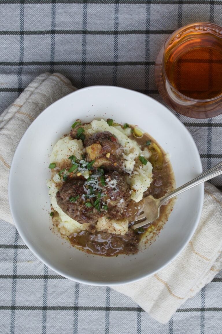 meatballs with meaty gravy served over mashed potatoes in white bowl on checked tablecloth