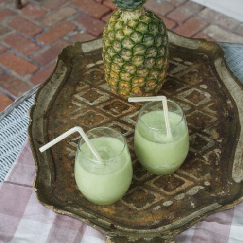 Two glasses of pineapple cucumber smoothie on tray with fresh pineapple