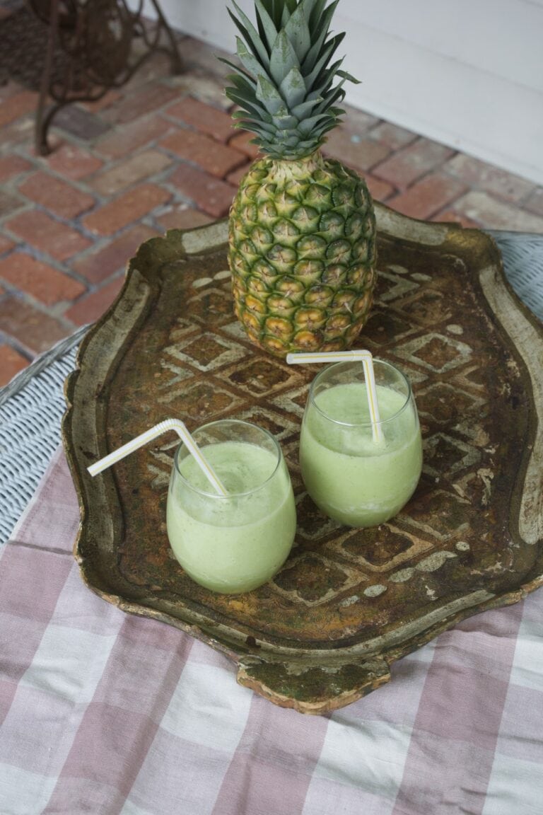 Two glasses of pineapple cucumber smoothie on tray with fresh pineapple