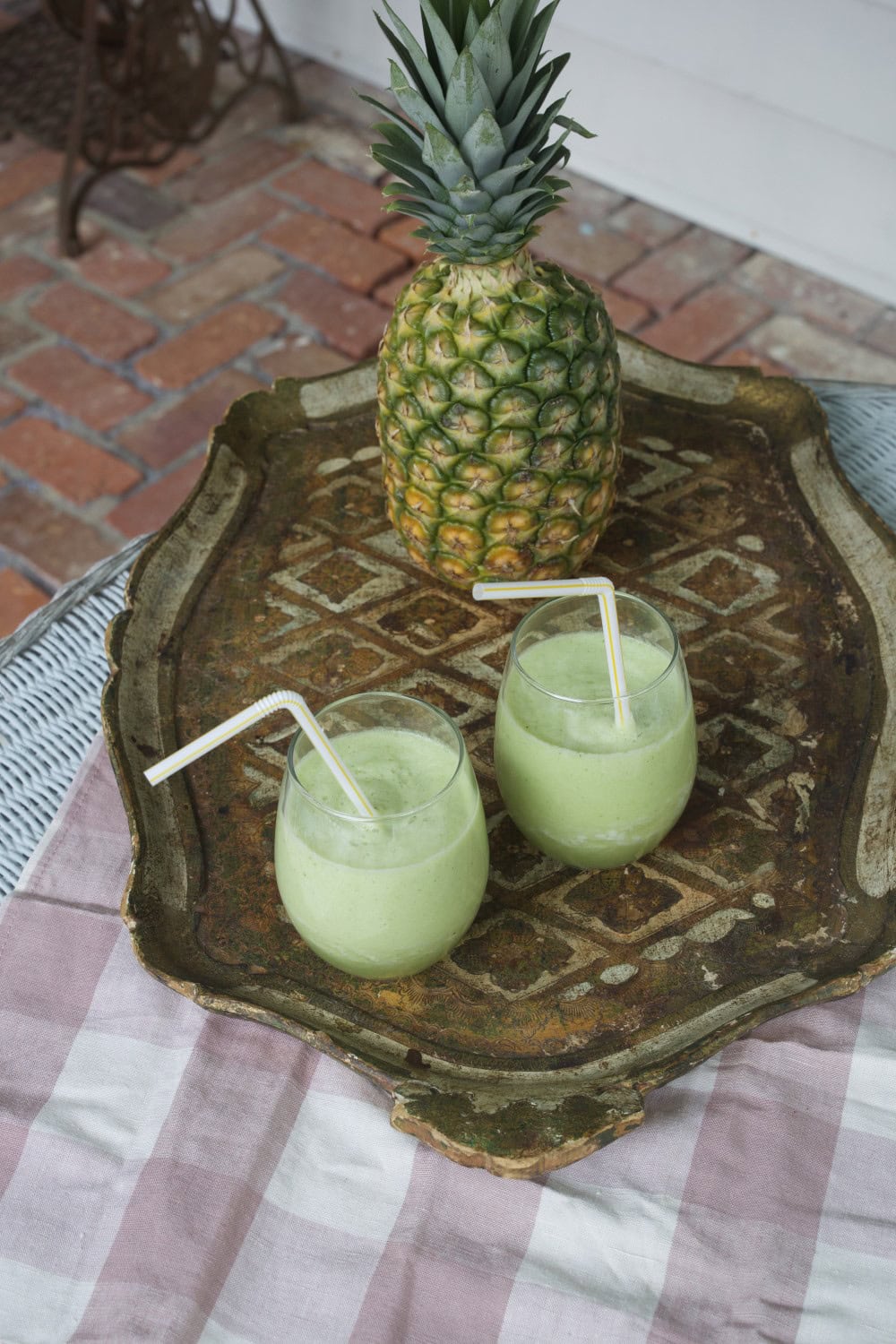 Two glasses of pineapple cucumber smoothie on tray with fresh pineapple