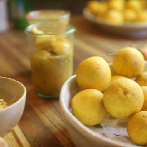 jar of preserved lemons alongside bowl of fresh lemons and small bowl of pasta on kitchen counter