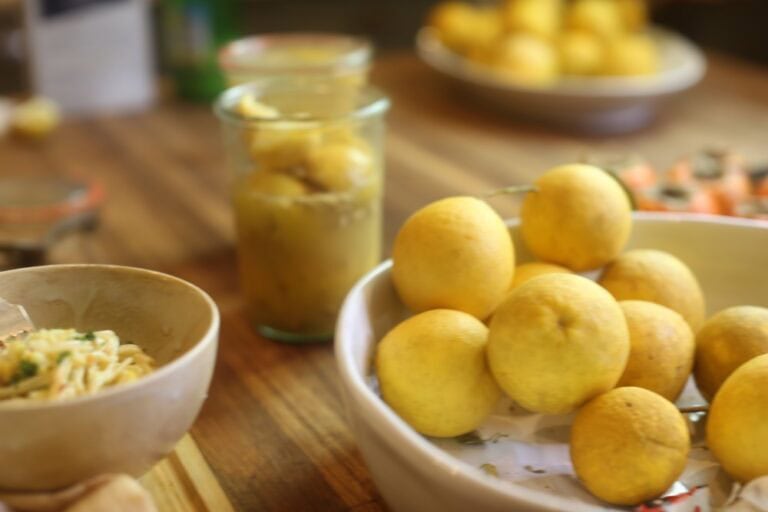 jar of preserved lemons alongside bowl of fresh lemons and small bowl of pasta on kitchen counter