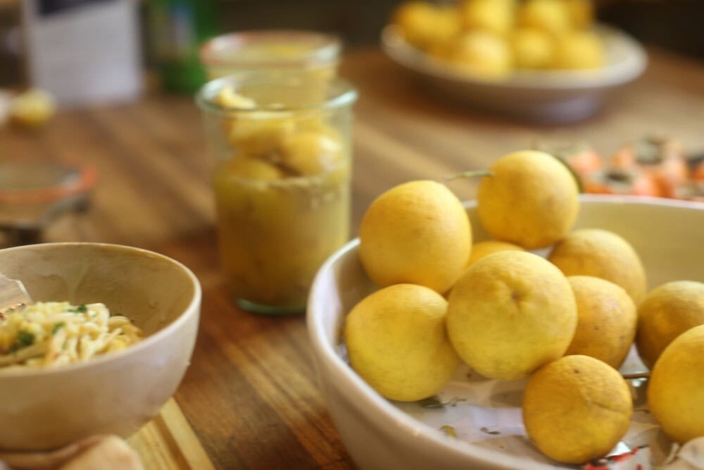 jar of preserved lemons alongside bowl of fresh lemons and small bowl of pasta on kitchen counter