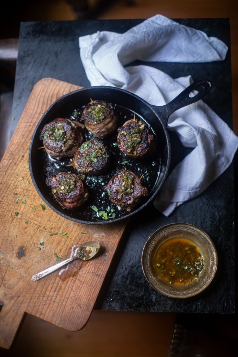 venison steaks / tenderloin medallions in cast iron pan on cutting board with dish of herb butter