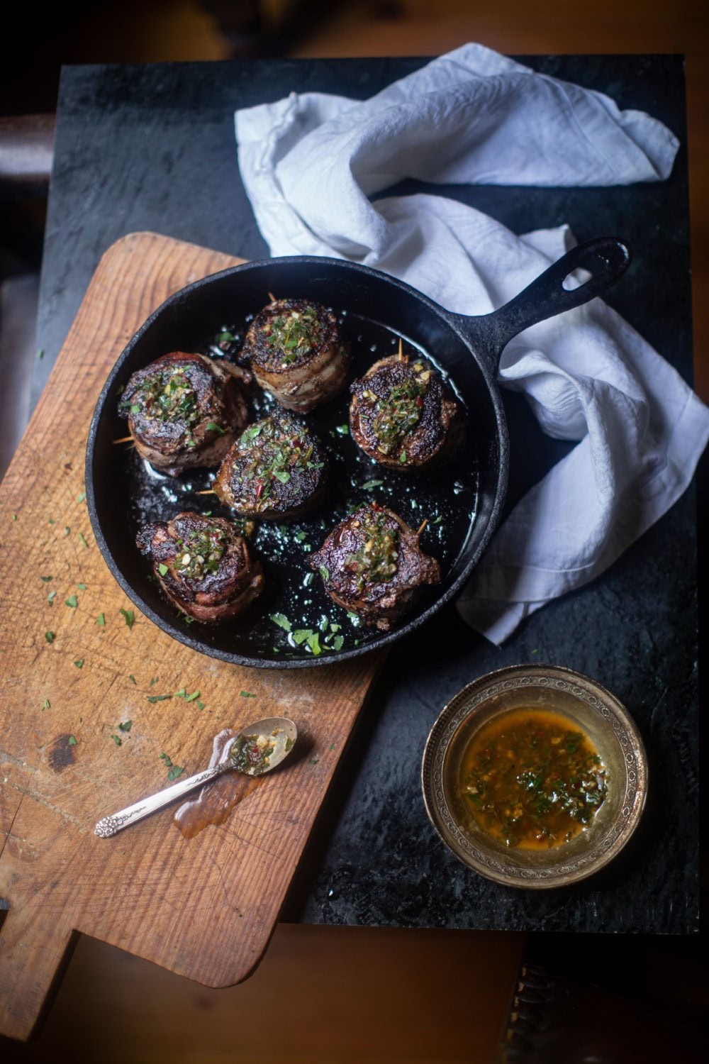 venison steaks / tenderloin medallions in cast iron pan on cutting board with dish of herb butter