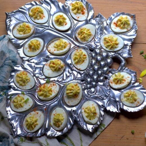 deviled eggs in silver platter on wooden counter, floral napkin below platter