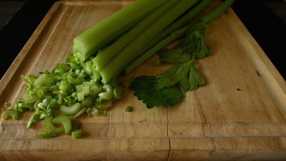 celery stalked on wooden cutting board, partially minced
