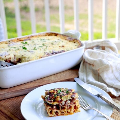 Pastitsio / Greek Lasagna - serving on white plate in front of large casserole dish outdoors