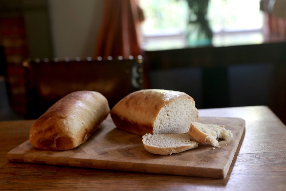 two homemade sourdough bread loaves on wooden cutting board with one loaf sliced