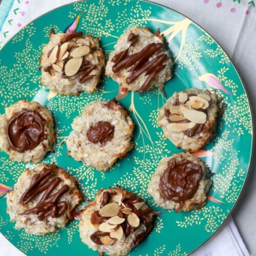 Fresh banana coconut cookies with almond slices and chocolate drizzle on a decorative plate.