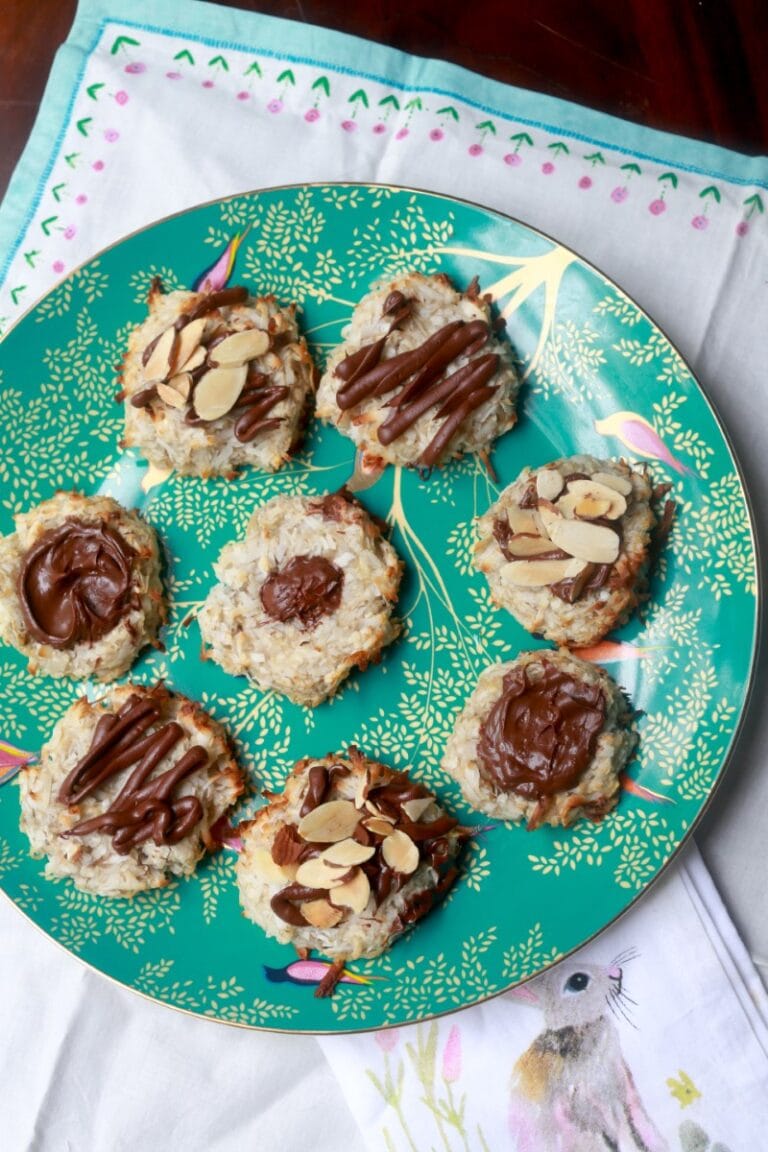Fresh banana coconut cookies with almond slices and chocolate drizzle on a decorative plate.
