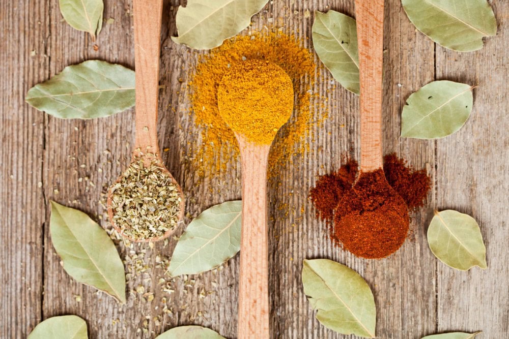 spices heaped in wooden spoons with leaves on wood counter