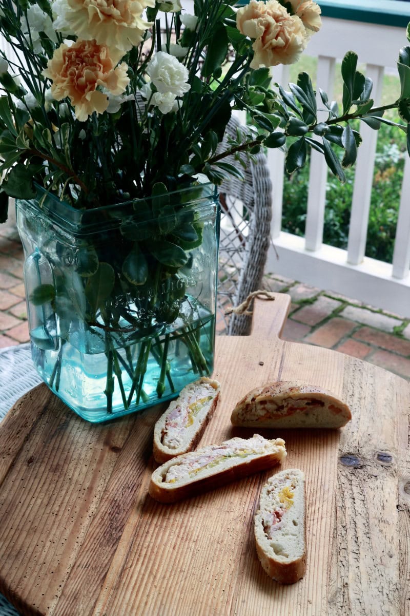 Sliced Italian stromboli - calzone sandwich on wood porch table in front of large vase of flowers